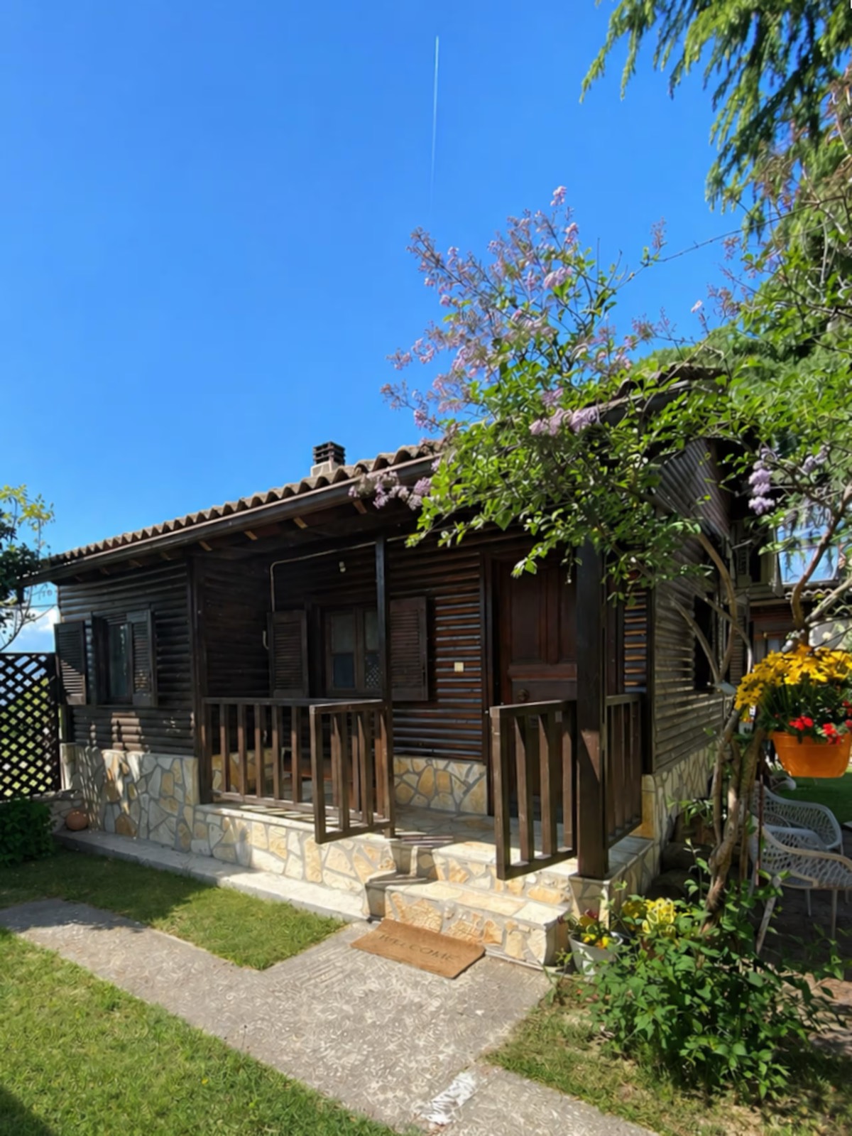 The Cozy Chalet's covered porch and stone steps, framed by a flowering vine against a clear sky.