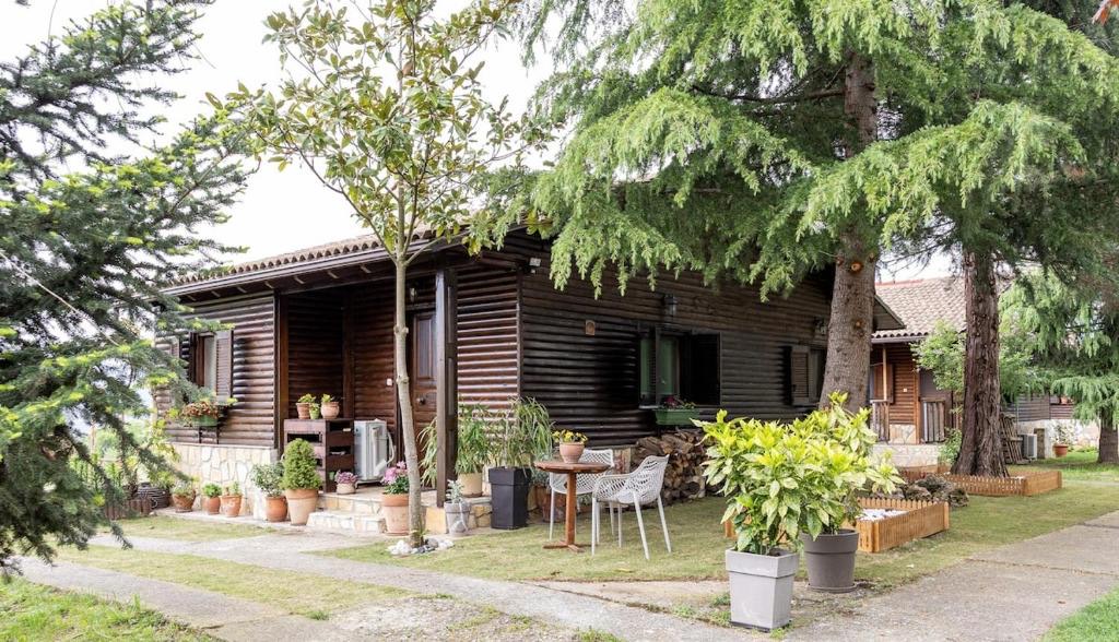 Το σαλέ από τον κήπο, με τραπέζι και καρέκλες στην πλακόστρωτη βεράντα κάτω από τα δέντρα.