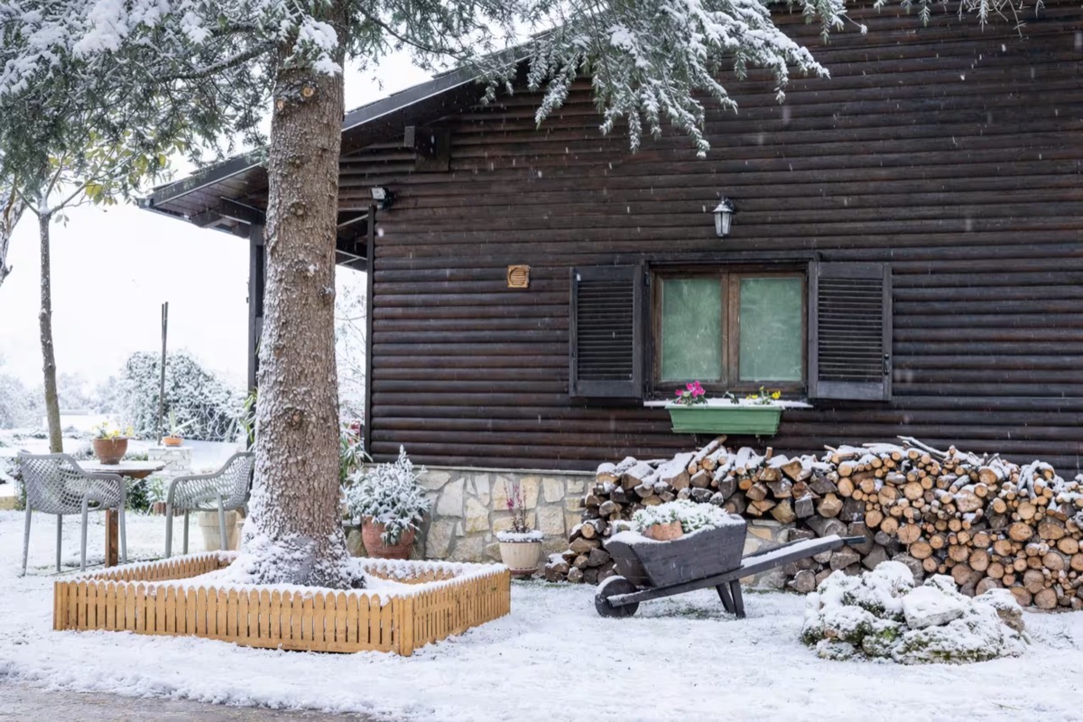 The Grand Chalet under snow, firewood stacked the length of the wall and a wheelbarrow standing on the cleared path.