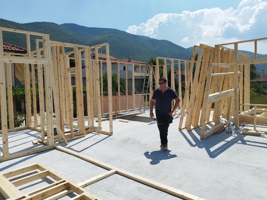 Τα γυμνά ξύλινα πλαίσια των τοίχων όρθια πάνω στη χυτή πλάκα, με τα βουνά στο βάθος.