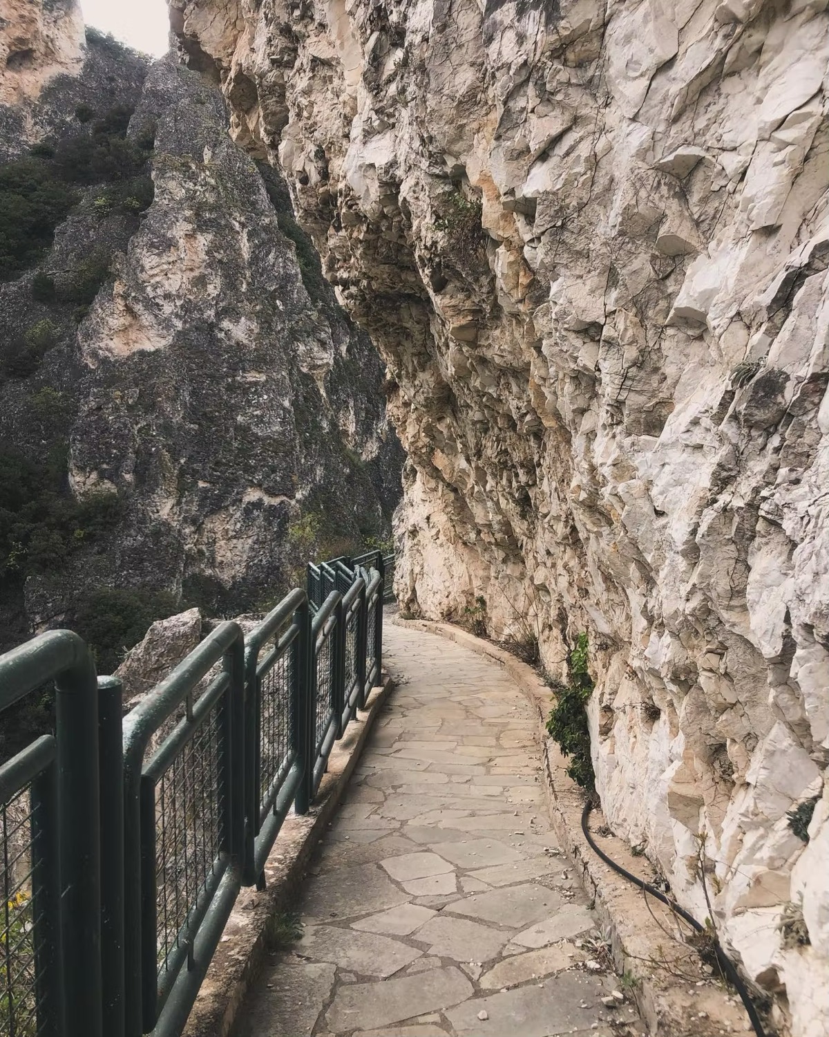 Ένα πλακόστρωτο μονοπάτι με σιδερένια κάγκελα, σκαμμένο στη βάση ενός βράχου.